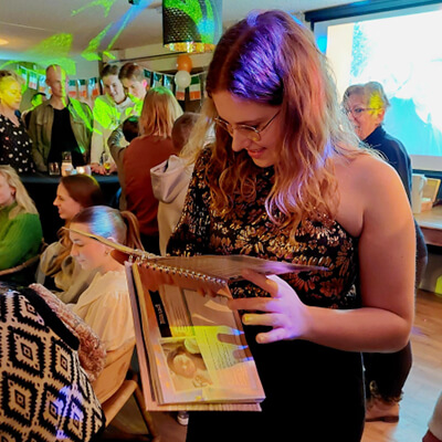 Vrouw kijkt vrolijk over haar schouder met een vriendenboek in haar handen